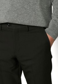 Svarta skräddarsydda byxor med en mjuk textur, dragkedja och knappstängning, sidofickor och sydda detaljer, i kombination med en grå tröja.