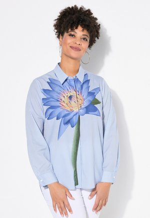 Gestreepte blauwe overhemden met een grote blauwe waterlelieprint op de voorkant, lange mouwen en een ontspannen pasvorm. Witte achtergrond.