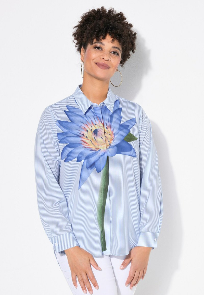 Camicia a righe blu con stampa di una grande ninfea blu sulla parte frontale, maniche lunghe e vestibilità comoda. Sfondo bianco.