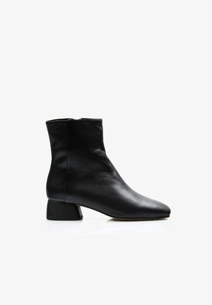 Bota de tobillo de cuero negro con punta afilada, diseño minimalista y tacón corto y grueso. Textura suave con una silueta elegante.