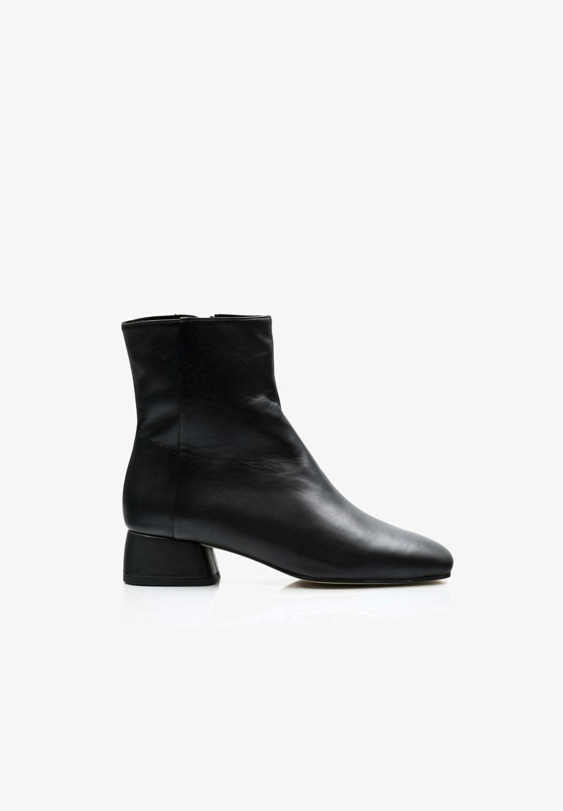 Bota de tobillo de cuero negro con punta afilada, diseño minimalista y tacón corto y grueso. Textura suave con una silueta elegante.