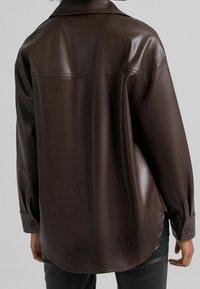 Brun konstläder skjorta med spetsad krage, långa ärmar och knappade manschetter, med en mjuk textur och en något böjd fåll.