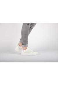 Weiße Sneakers aus einer Mischung aus glatten und strukturierten Materialien, mit Schnürdesign und gepolsterter Sohle, kombiniert mit grauen umgekrempelten Jeans.