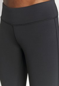 Gros plan sur une personne portant un legging de sport noir taille haute, montrant des coutures flatlock et un tissu lisse et extensible sur les hanches et les cuisses.