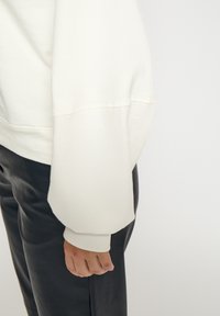 Cremekleurige sweatshirt met oversized mouwen en geribbelde manchetten. Gecombineerd met zwarte broek, met een gladde textuur en een ontspannen pasvorm.