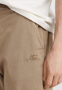 Beige bomuldsbukser med sidelommer og et broderet logo. Stof er blødt med en afslappet pasform.