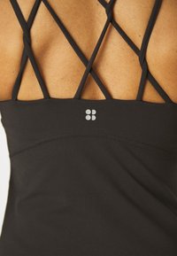 Černý sportovní top s křížovým designem ramínek na zadní straně. Hladká textura s jemným logem nad lemem.