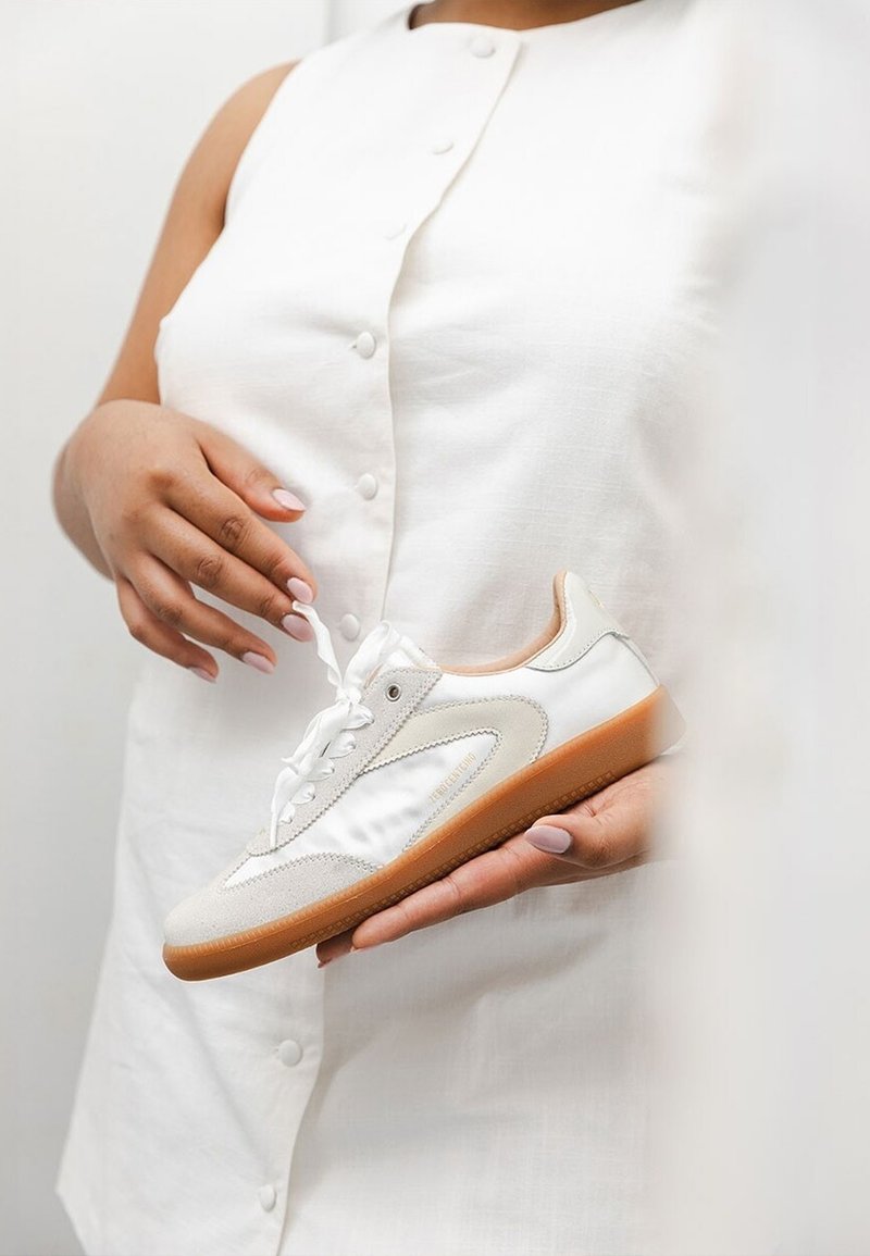 Vit sneaker med en blandning av matta och blanka texturer, med en krämfärgad mockadetalj, platta snören och en gummisula.