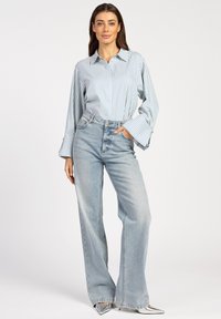 Light blue striped shirt with wide sleeves, paired with high-waisted, wide-leg light wash jeans and silver pointed-toe heels.