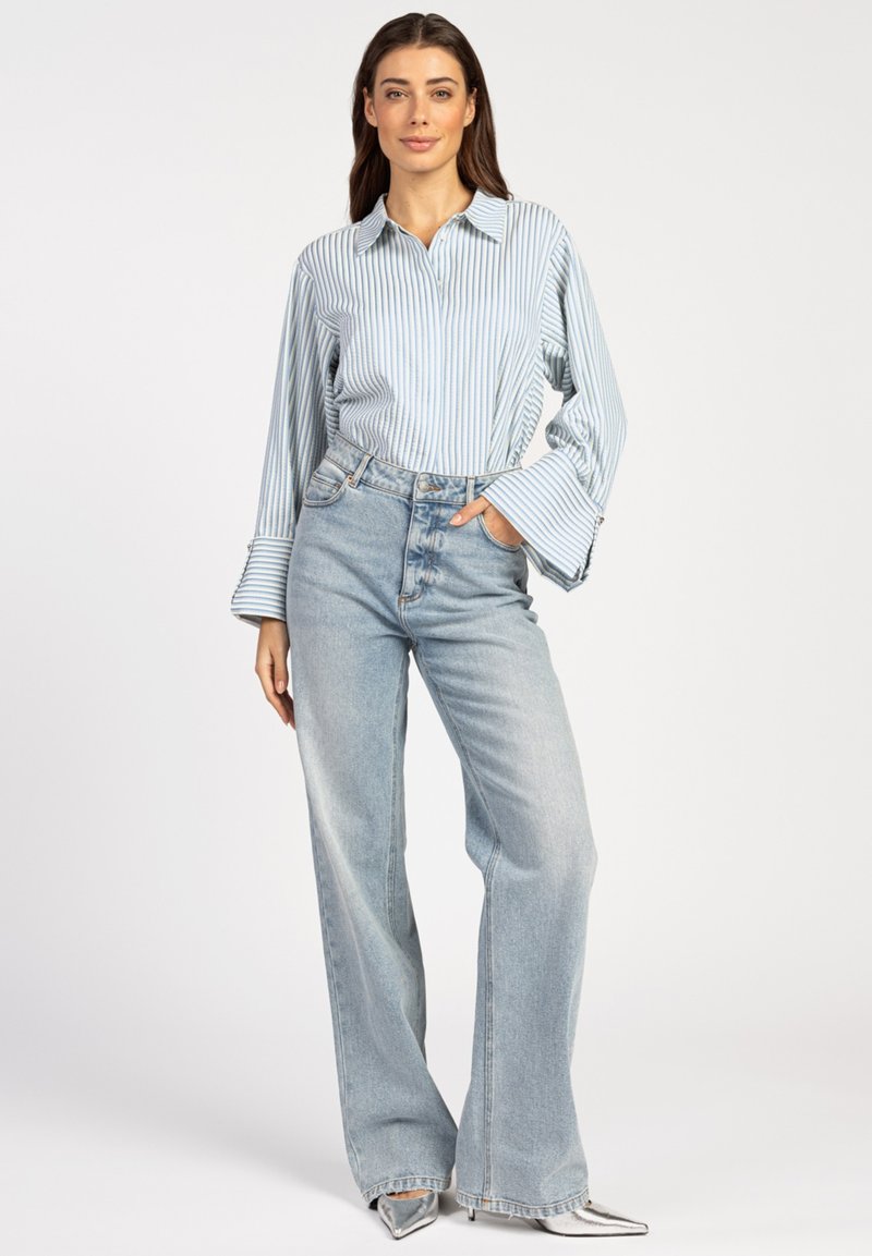 Light blue striped shirt with wide sleeves, paired with high-waisted, wide-leg light wash jeans and silver pointed-toe heels.