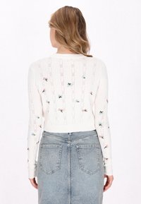 Pulover alb, tricotat, cu broderie florala si dungi orizontale. Maneci lungi, mansete cu nervuri si un design scurt. Asortat cu o fusta din denim.