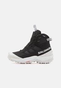 Czarne buty trekkingowe wykonane z materiału syntetycznego, o wysokim kroju, z białą podeszwą i teksturowanymi akcentami, oznaczone napisem "SALOMON."