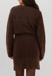 Bruine gebreide sweaterjurk met een cropped ontwerp. Heeft lange mouwen en een gestructureerde afwerking. Gladde onderzoom, aansluitende taille.