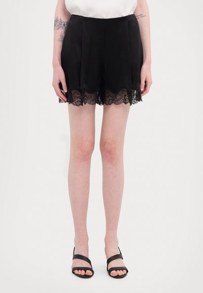 Shorts noirs en tissu lisse avec un ourlet en forme de feston et une bordure en dentelle. Design ajusté avec des plis à l'avant pour plus de détails.