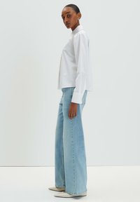 White long-sleeve shirt with a pointed collar, paired with light blue wide-leg jeans and beige pointed-toe flats. Smooth fabric and relaxed fit.
