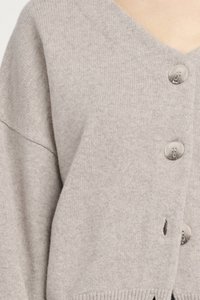 Cardigan grigio chiaro, lavorato a maglia, con scollatura a V e tre bottoni, caratterizzato da polsini a coste e una piccola apertura sull'orlo. Texture morbida.