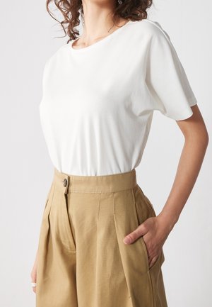 Hvid bomulds-T-shirt kombineret med højtaljede, beige plisserede bukser med knapdetalje og sidelommer. Glat tekstur og afslappet pasform.