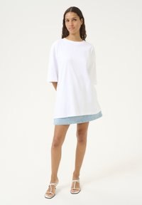 Witte oversized T-shirt met korte mouwen, gecombineerd met een lichtblauwe denim minirok en witte sandalen met een dunne bandjesdesign.