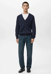Navy knitted cardigan with a V-neck, button closure, ribbed texture, paired with blue denim jeans and black shoes.