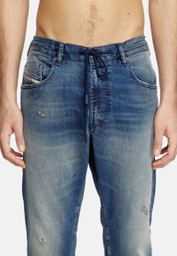 Pantalons jogger en denim bleu, avec une taille à cordon de serrage, des détails usés et deux poches avant avec des coutures visibles et un effet décoloré.