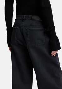 Zwarte jeans met hoge taille en een ontspannen pasvorm, voorzien van twee achterzakken en een leren merkembleem op de tailleband. Zachte denimtextuur.