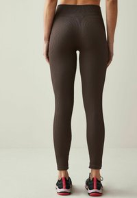 Brune geribbelde legging met een hoge tailleband, aansluitend ontwerp en enkel lengte, gecombineerd met zwarte sportieve schoenen met rode accenten.
