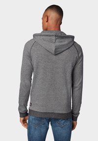 Grijze hoodie van een gestructureerde stof, met een buidelzak en ribgebreide manchetten en zoom, gedragen over blauwe spijkerbroeken.