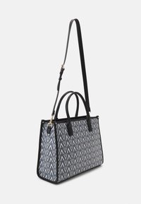 Sac fourre-tout avec motif zigzag marine, accents en cuir noir, anses supérieures doubles et une bandoulière amovible. Forme rectangulaire robuste.