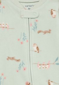 Lys grønn fleece baby jumpsuit med knappelukking, med et mønster av fugler, ekorn og blomster i rosa og brune toner.
