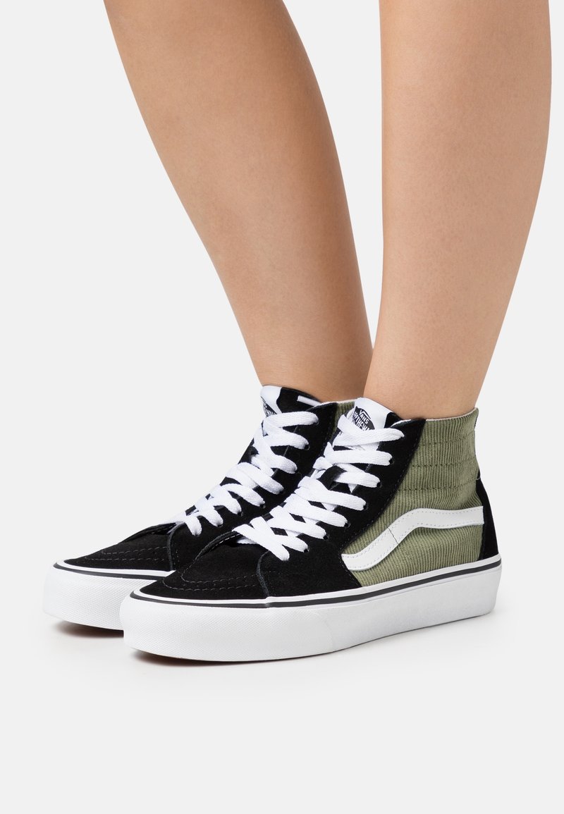 Baskets montantes en daim noir avec un tissu côtelé vert olive, des lacets blancs et une bande latérale blanche classique.