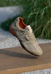 Beige joggesko med nettingpaneler, snøring og røde interiørdetaljer. Har svart gummisåle og Geox-logo på tungen.