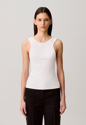 Top bianco senza maniche con scollo rotondo, realizzato in tessuto liscio, con ricamo logo discreto sul petto, abbinato a pantaloni neri.