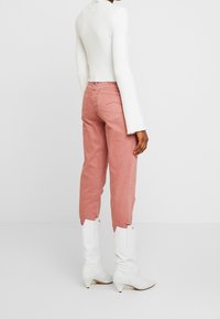 Hellrosa Hose mit schmal zulaufendem Bein und verkürztem Schnitt, kombiniert mit einem weißen, gerippten Langarmshirt und weißen, strukturierten Cowboy-Stiefeln.