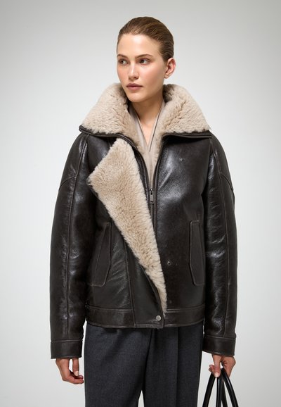 Braune leren jas met een brede beige schapenvachtkraag, ritssluiting en zijzakken. Zachte textuur en oversized silhouet.