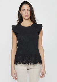 Haut en coton noir avec des manches courtes à volants, broderie florale sur le devant, et un ourlet en dentelle avec des découpes.