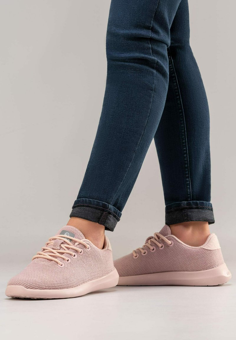 Rosa Strick-Sneaker mit strukturiertem Obermaterial, abgerundeter Zehenkappe und weichem Fersenbereich. Ausgestattet mit hellrosa Schnürsenkeln und flexibler Sohle. Getragen mit dunklen Jeans.