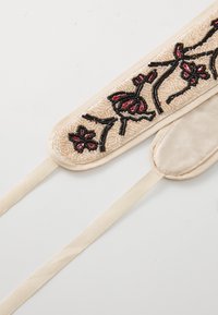 Masca de somn cu mărgele, cu design floral în nuanțe de roz și negru, pe un material bej. Are panglici din satin și o textură netedă, moale.