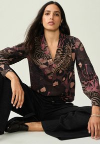 Garš sleeve blouse ar maisītu dzīvnieku rakstu rozā, brūnā un melnā krāsā; viegla auduma; dziļa V formas kakla izgriezums; saskaņota ar melnām teksturētām biksēm.
