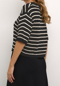 Maglione lavorato a maglia a righe nere e crema con maniche corte, caratterizzato da un colletto e un orlo inferiore a coste, mostrato di lato.