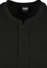 Svart henley-skjorte med rund hals, knapplist og teksturert stoff. Har to sorte knapper og et merkeetikett ved kragen.