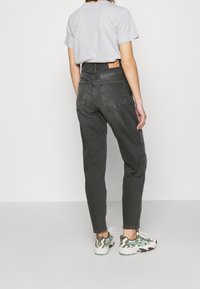 Vysokém pasu černé džíny z denimu s zúženým střihem, obsahující zadní kapsy a koženou štítek. V kombinaci se šedým tričkem a teniskami.