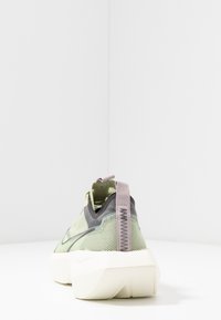 Baskets avec une tige en mesh vert translucide, des accents gris et une semelle blanche épaisse. Présente une languette de traction lavande avec une couture texturée.