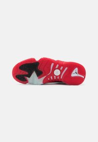 Semelle de sneaker rouge et noire avec un motif en chevrons, en caoutchouc texturé, et des accents translucides. Présente des éléments circulaires et striés.
