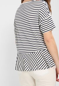 Pasiasty top z krótkim rękawem w kolorze kremowym i granatowym, z peplum z tyłu, pionowymi paskami, gładką fakturą i luźnym krojem.