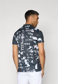 Sötét szürke, rövidujjú pólóing fehér absztrakt szöveggel és grafikákkal. Klasszikus gallér és slim fit fazon jellemzi.