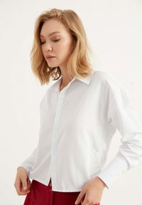 Camicia bianca con colletto classico e maniche lunghe, caratterizzata da una vestibilità rilassata e un tessuto leggero e morbido.