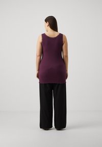Top in cotone viola a costine con bordo in pizzo sagomato, abbinato a pantaloni neri larghi. Design semplice, aderente in vita, che allunga la silhouette.
