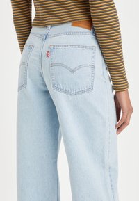 Ljusblå högmidjade jeans med en avslappnad passform, som har två bakfickor och en läderlogotyp på midjebandet. Mjuk denimtextur.