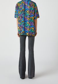 Camisa de manga corta y corte holgado en vibrantes patrones geométricos de azul, morado y amarillo, combinada con pantalones acampanados negros que presentan una textura desgastada.