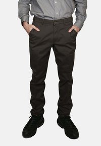 Pantaloni marrone scuro dal taglio slim, con fronte piatto, tasche laterali e passanti per cintura, abbinati a sneakers nere e una camicia a fantasia.